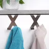 Two metal 'X' shaped hooks are mounted below a shelf, one holding a blue towel and the other a beige towel. Anteprima dell’immagine prodotto