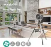A modern living room with a fireplace, sofa, and large windows, featuring a metal tripod fan. Produktbild-Vorschau