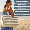 A woman on a beach holding a striped beach bag. Produktbild-Vorschau