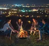 People gathered around a fire pit at night with city lights in the background. Náhled obrázku produktu