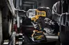 A person wearing black gloves is using a DeWALT cordless impact wrench to tighten a bolt on a piece of machinery. Podgląd zdjęcia produktu