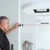A man is using a laser distance measurer to measure a wall in a room that appears to be under construction. Voir les images du produit