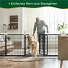 An elderly man is walking two golden retriever dogs through a black metal pet gate in a living room. Produktbild-Vorschau