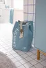 A blue laundry basket with the word "Laundry" printed on it, placed on a tiled floor in a bathroom. Náhled obrázku produktu