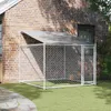 A dog kennel with a roof and door is set up on a grassy lawn next to a brick house. Produktbild-Vorschau