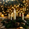 A festive arrangement of LED candles and pine branches on a wooden table, with blurred bokeh lights in the background. Náhled obrázku produktu