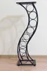 A black metal wine rack with a curved design, standing on a wooden floor against a white wall. Anteprima dell’immagine prodotto