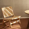 A rattan armchair is placed on a patterned rug next to a round wooden table, with sunlight casting striped shadows across the scene. Náhľad obrázku produktu