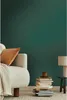 A cozy living room scene with a sofa, throw blanket, pillow, stack of books, and a lamp. Produktbild-Vorschau