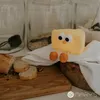 A cute cheese-shaped night light sits on a white cloth next to a loaf of bread on a wooden cutting board. Jars of food are in the background. Podgląd zdjęcia produktu