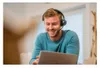 A man wearing a headset is smiling while looking at a laptop. Voir les images du produit