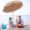 A couple relaxing on a beach under a fringed umbrella, with a guitar and beach bag nearby. Produktbild-Vorschau