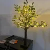 A decorative artificial tree with LED lights sits on a black surface, possibly a piece of furniture or electronic equipment. Produktbild-Vorschau