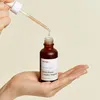 A hand holding a bottle of serum with a dropper above it. Voir les images du produit