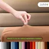 A hand is stretching a nougat-colored fitted sheet, showcasing its elasticity. Below, a row of different colored fitted sheets are displayed. Produktbild-Vorschau