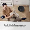 A man is relaxing and reading a book while a robot vacuum cleaner operates in the background. Voir les images du produit