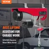 A red electric steel wire hoist is mounted on a dark bar, with a blurred background of a garage and a car. Náhľad obrázku produktu