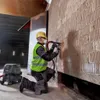 A construction worker is using a power tool to cut into a brick wall, with a vacuum cleaner attached. Produktbild-Vorschau