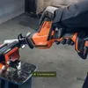 A person wearing gloves is holding an orange and black reciprocating saw, cutting into a metal object clamped in a vise. Produktbild-Vorschau