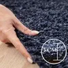 A hand is shown pressing into a thick, navy blue shaggy rug, with a circular graphic indicating the rug's thickness. Produktbild-Vorschau