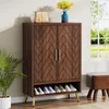 A wooden shoe cabinet with a herringbone pattern on the doors, placed in a room with a plant and a window in the background. Náhľad obrázku produktu