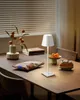 A table lamp is placed on a wooden table with some food items and a vase of flowers. Produktbild-Vorschau