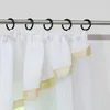 A close-up view of white sheer curtains with a gold ribbon trim, hanging from a metal curtain rod with black rings. Produktbild-Vorschau