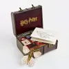 An open trunk filled with miniature Harry Potter books and a letter, with a butterfly-shaped brooch in the foreground. Produktbild-Vorschau