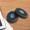 Two black ear pads with blue striped circular logos are placed on a wooden surface next to a white tablet and some papers. Náhled obrázku produktu