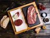 A top-down view of a steak cooking set on a wooden table, with ingredients and bread. Produktbild-Vorschau