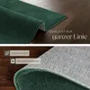 A close-up view of a green rug, showing its texture and underside, with text overlays highlighting quality and features. Produktbild-Vorschau