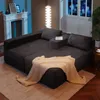 A dark gray sectional sofa with a beige throw blanket draped over it, set in a living room with a fireplace and a tall floor lamp. Produktbild-Vorschau