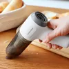 A hand holding a white and gray handheld vacuum cleaner over a wooden surface with bread crumbs. Produktbild-Vorschau
