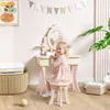 A young girl is sitting at a pink vanity table with a stool, playing with makeup accessories. Produktbild-Vorschau