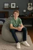 A young boy sits on a large, dark gray beanbag chair in a bedroom setting. Voir les images du produit