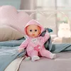 A baby doll sitting on a bed with pillows and blankets. Náhled obrázku produktu