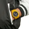 A person wearing a yellow Casio G-Shock watch on their wrist, partially obscured by a jacket. Náhled obrázku produktu