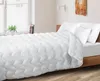 A bed with white bedding, including a comforter and pillows, in a room with a window and a plant. Voir les images du produit