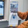 A person is holding a mini penguin-shaped water dispenser with a water bottle on top. Produktbild-Vorschau