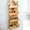 A wooden wall shelf with four tiers, decorated with small items like jars, a decorative sphere, and greenery. Produktbild-Vorschau