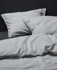 A close-up view of a bed with gray bedding and pillows against a dark background. Produktbild-Vorschau