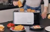 A person is placing waffles into a ZEEGMA toaster, with other food items like tomatoes and bread on the counter. Voir les images du produit