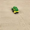 A toy John Deere farm vehicle is on a sandy surface, leaving tire tracks. Produktbild-Vorschau