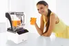 A woman is drinking a smoothie next to a blender. Anteprima dell’immagine prodotto