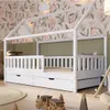 A child's bedroom with a white house-shaped bed, decorated with floral wallpaper and green wall panels. Toys are scattered on the floor. Produktbild-Vorschau