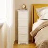 A narrow white cabinet with four drawers stands next to a bed with a yellow headboard in a bedroom setting. Produktbild-Vorschau