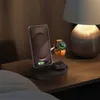 A bedside table with a wireless charging station holding a smartphone, smartwatch, and earbuds, next to a lamp. Podgląd zdjęcia produktu