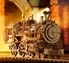 A detailed wooden model of a steam locomotive sits on tracks, illuminated by warm, dramatic lighting. Náhľad obrázku produktu