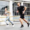 A man and a woman are running outdoors, wearing athletic gear and ankle weights. Produktbild-Vorschau