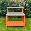 A gardening workbench is placed outdoors on a lawn in front of a green hedge with pink flowers. Anteprima dell’immagine prodotto